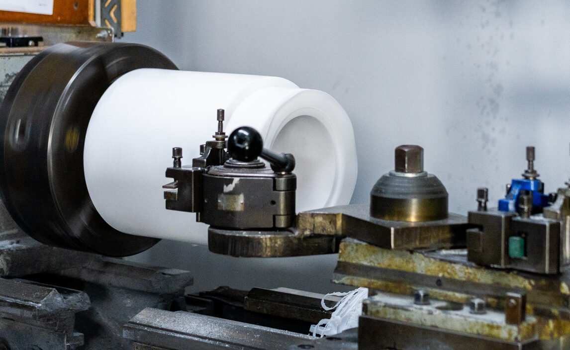 A metal lathe machine shaping a white cylindrical object, with digital displays above the lathe.