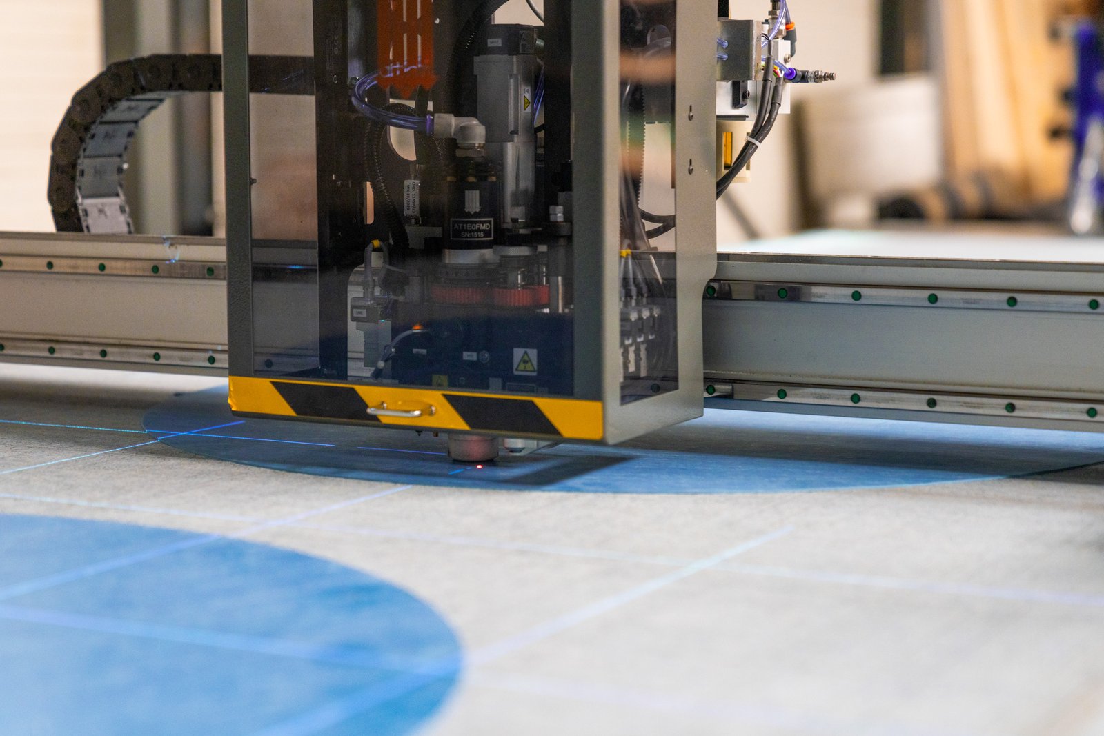Close-up of an industrial machine cutting or marking precise blue lines on a gray surface.