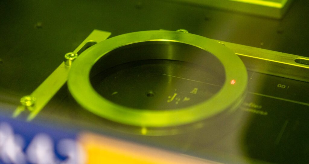 A metal ring being manufactured inside a 3D printer with a yellow-green light.