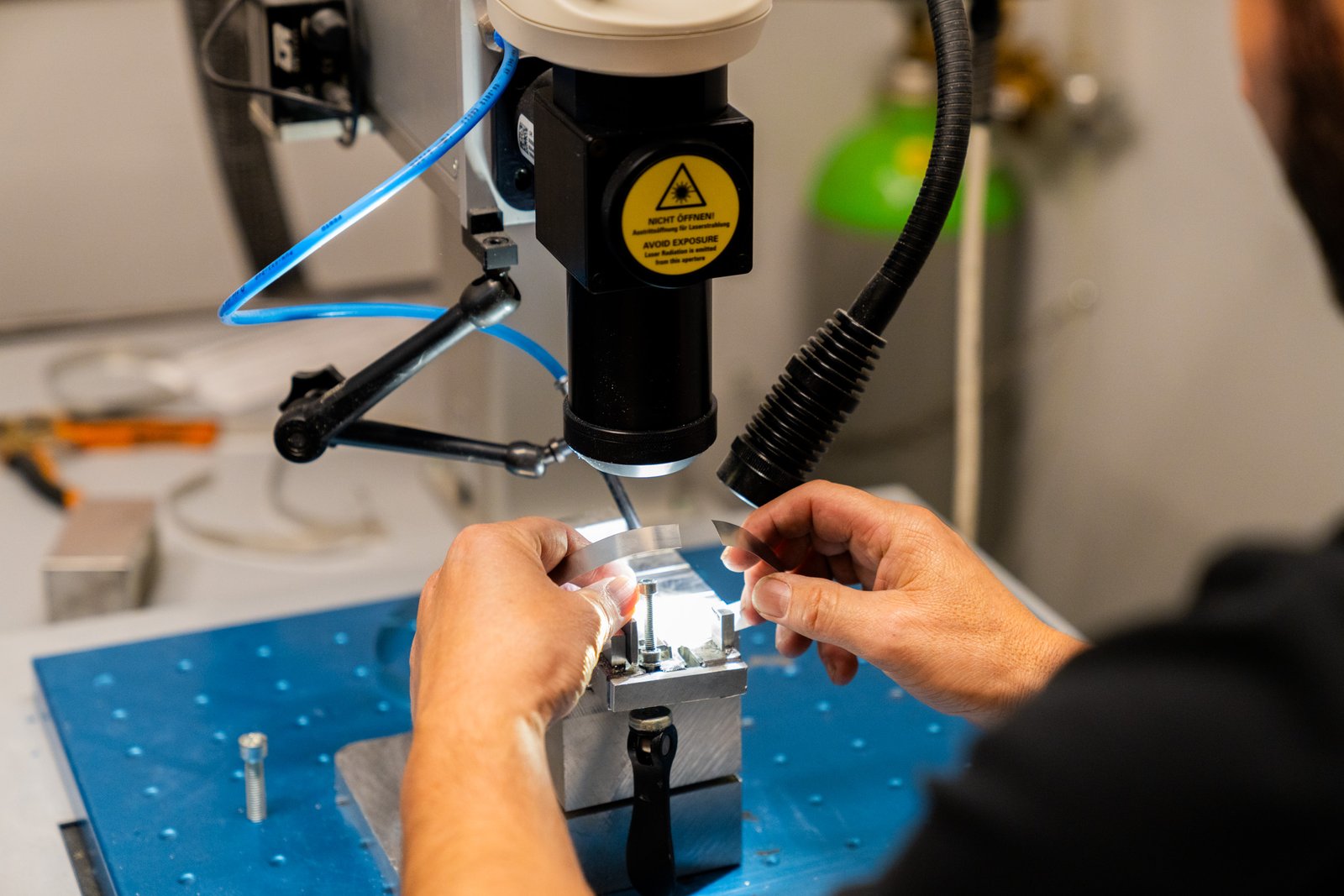 Person using a microscope and tools to work on a small electronic component in a laboratory setting.