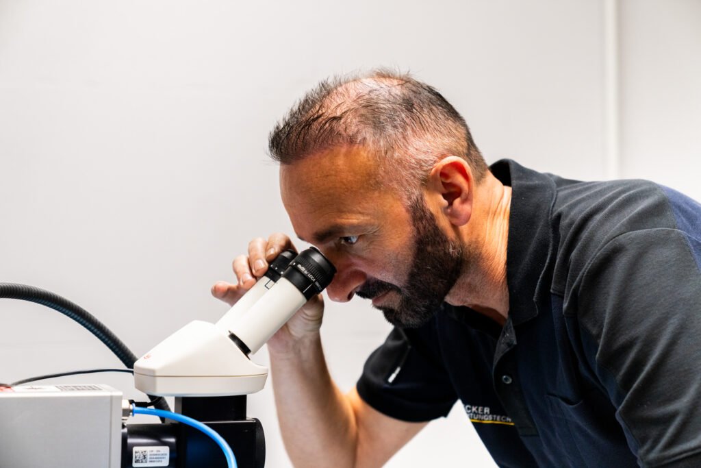A man with a beard looks into a microscope in a laboratory setting.