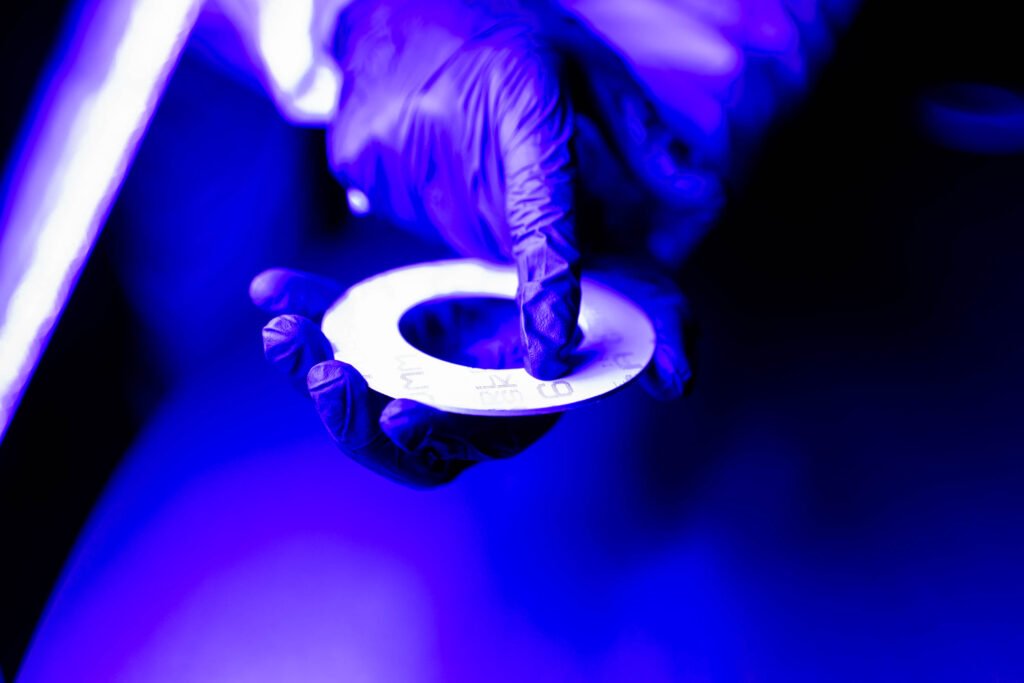 A gloved hand holds a circular object under blue and purple lighting.