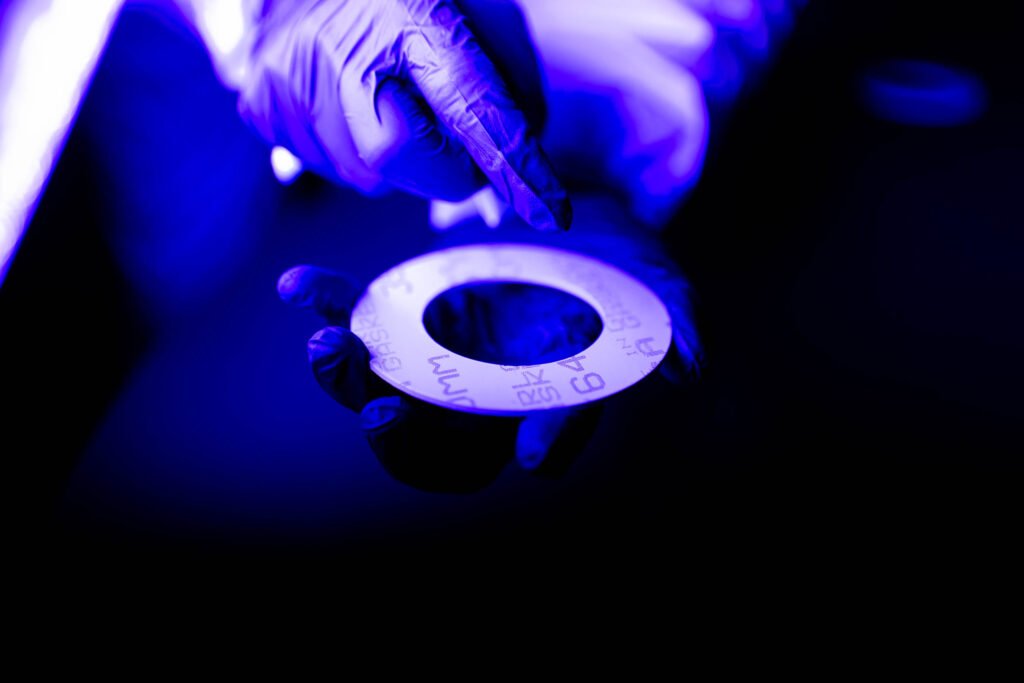 A gloved hand holds a circular object with markings, illuminated by blue and purple light.