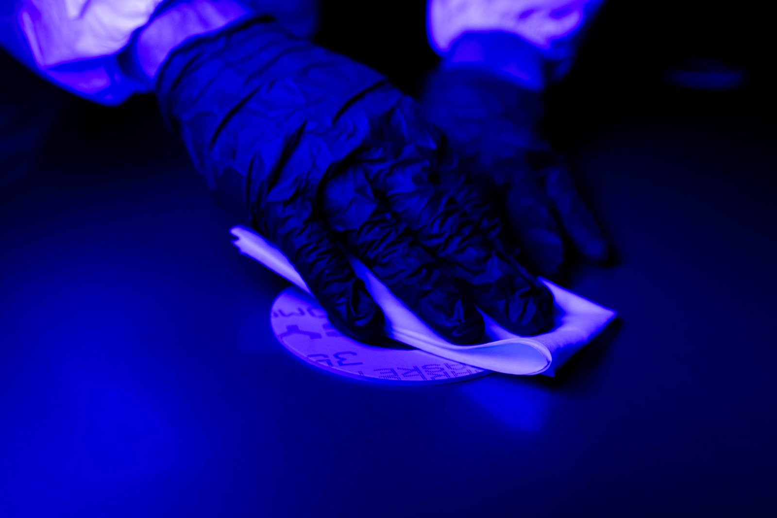 Gloved hands wiping a surface under blue light, suggesting cleaning or forensic inspection.